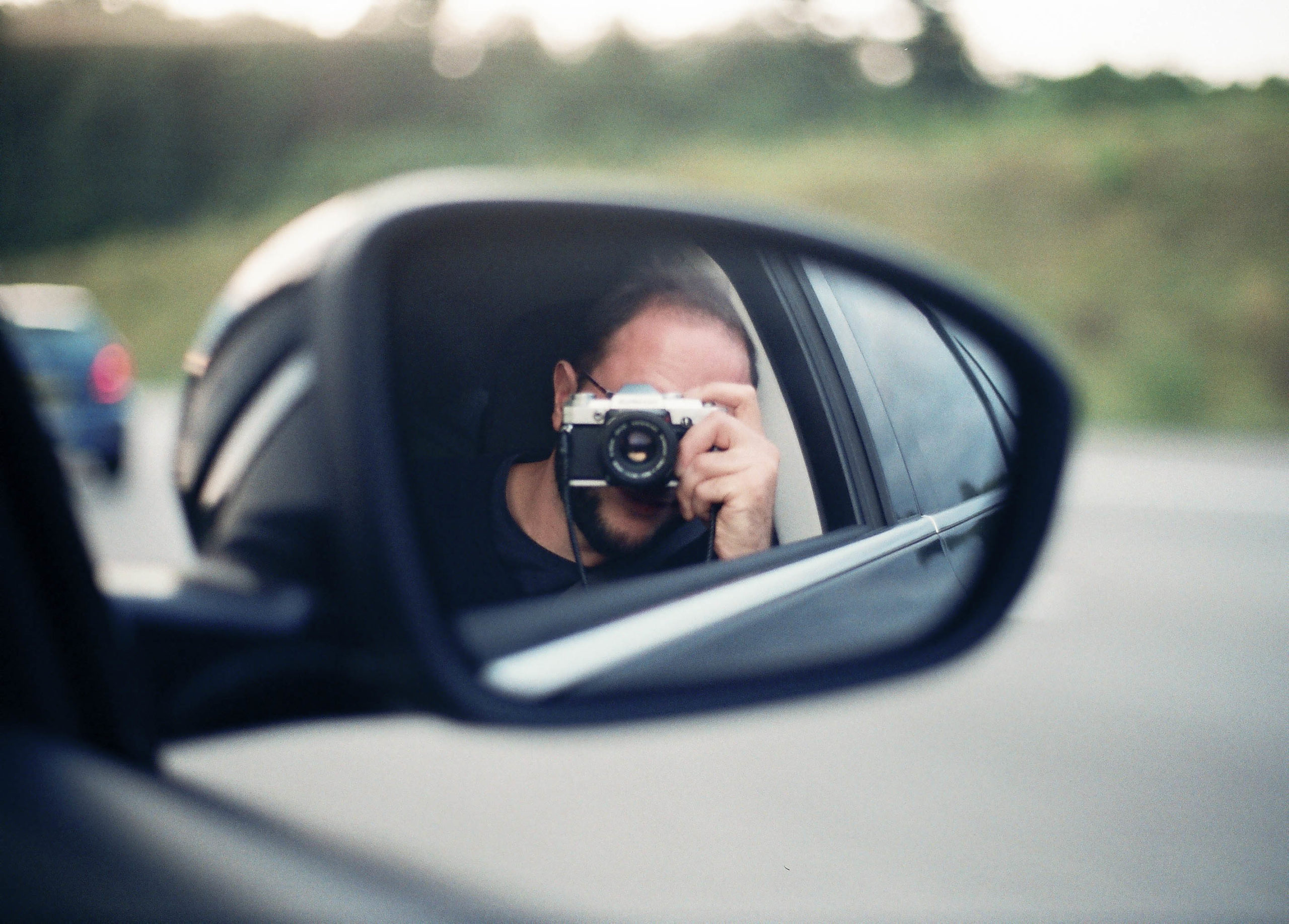 Mensch mit Kamera im Seitenspiegel eines Autos auf der Fahrt